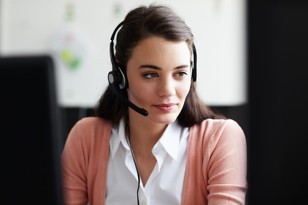 Trabajadora joven y concienzuda Una mujer joven y bonita con auriculares mirando la pantalla de su computadora