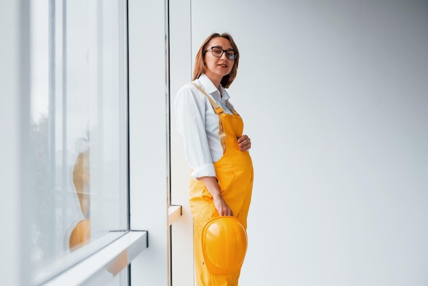 Trabajadora o ingeniera con uniforme amarillo y casco de pie en el interior