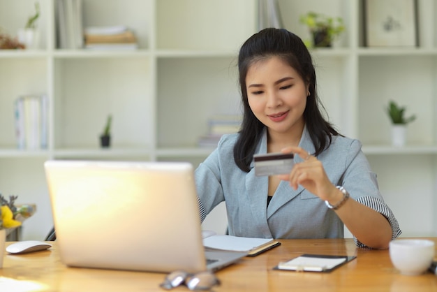 Una trabajadora o mujer de negocios que tiene una tarjeta de crédito y usa una computadora portátil en la mesa de su oficina