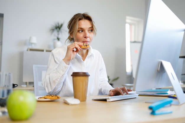 Trabajadora de oficina empresaria hambrienta comiendo galletas mientras trabaja en la computadora