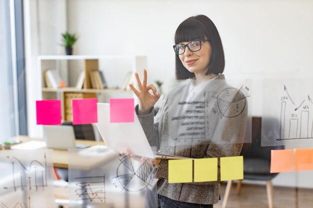 Trabajadora de oficina con gafas y traje elegante usando una tableta digital en compañía