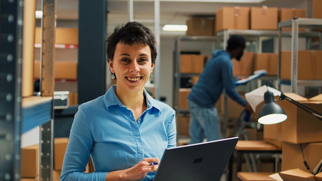 Foto trabajadora revisando paquetes de cartón de los estantes de la sala de almacenamiento, usando una computadora portátil para planificar el inventario de existencias y tomar notas. emprendedor que trabaja en el desarrollo de negocios y la cadena de suministro.