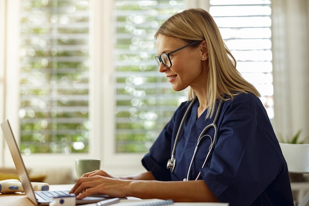 Foto trabajadora de la salud haciendo papeleo y usando una computadora portátil mientras trabaja en el consultorio médico