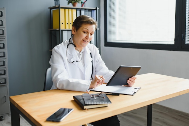 Trabajadora de la salud sonriente haciendo papeleo y usando una computadora portátil mientras trabaja en el consultorio del médico