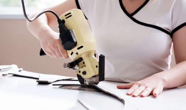 Trabajadora utiliza máquina de corte eléctrico de tela. Línea de producción de la industria textil.