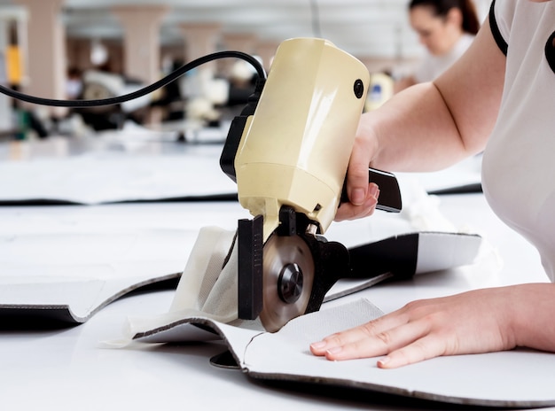 Trabajadora utiliza máquina de corte eléctrico de tela. Línea de producción de la industria textil.