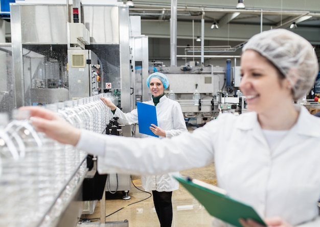 Trabajadoras en fábrica de embotellado comprobando las botellas de agua antes del envío. Control de calidad de inspección.