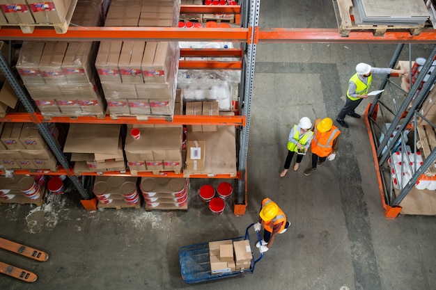 Uno de los trabajadores del almacén empuja el carro con cajas mientras que otros hacen revisión de mercancías