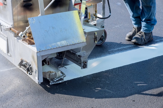 Los trabajadores aplican pintura blanca a una carretera que marca las rayas con un polvo reflectante sobre el nuevo asfalto