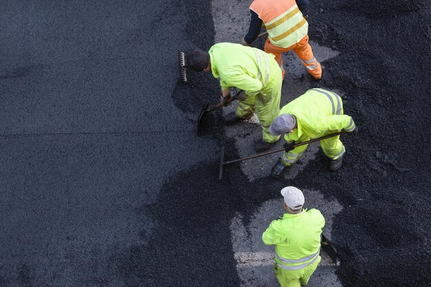 Los trabajadores durante el asfaltado de obras viales en las calles de la ciudad. Pavimentación de asfalto. Vista de ángulo alto. Copia espacio