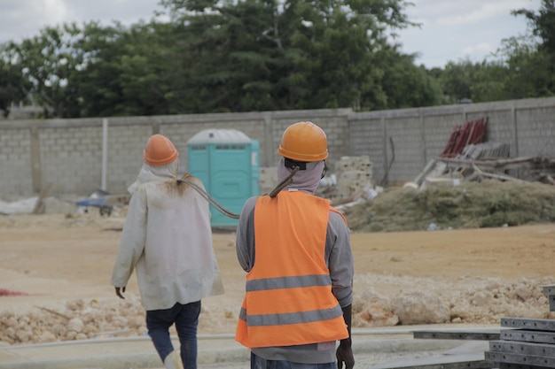 Trabajadores com trajetórias de proteção na construção llevan grupo de barillas de acero em conjunto, vista trasera