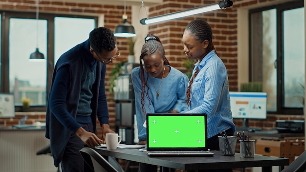 Trabajadores con computadora portátil con pantalla verde, usando una pantalla de maqueta en blanco para revisar las estadísticas anuales de datos en la oficina. Colegas en equipo comprobando informes, trabajando con una pantalla de tecla croma aislada. Fotografía de trípode.