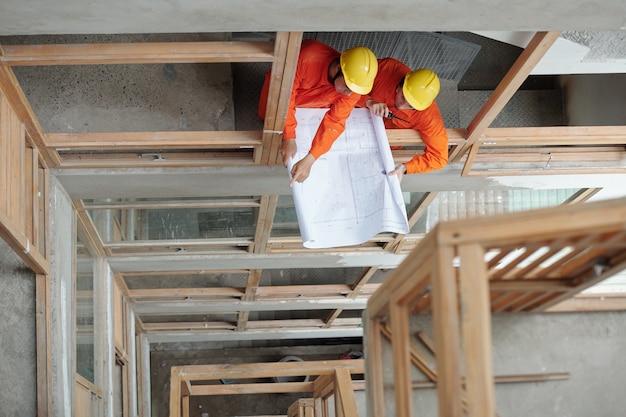 Trabajadores de la construcción discutiendo el plan de la casa y decidiendo qué piso renovar primero