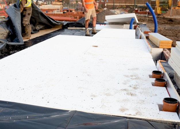 Los trabajadores de la construcción están colocando membranas impermeables y aislamiento por debajo del piso, para reducir la pérdida de calor en el futuro, durante la construcción de una nueva casa residencial.