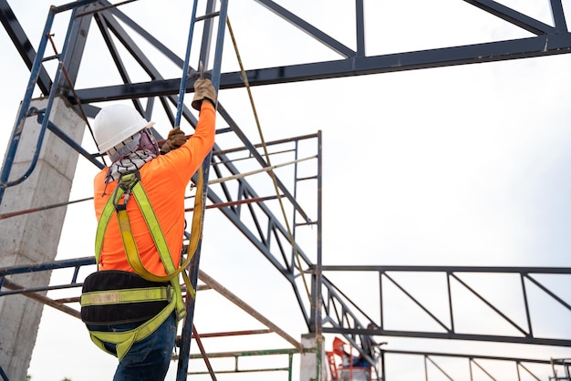 Los trabajadores de la construcción están trabajando en armazones de techo de acero con un dispositivo de detención de caídas para trabajadores con ganchos para arnés de cuerpo de seguridad en el sitio de construcción