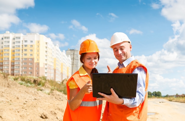 Trabajadores de la construcción masculinos y femeninos mirando portátil de casas en construcción