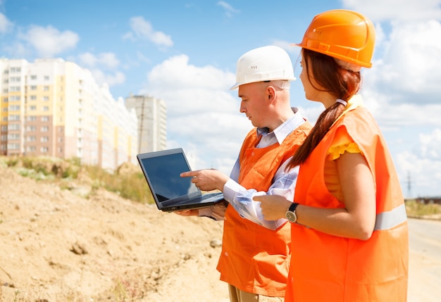 Trabajadores de la construcción masculinos y femeninos mirando portátil de casas en construcción