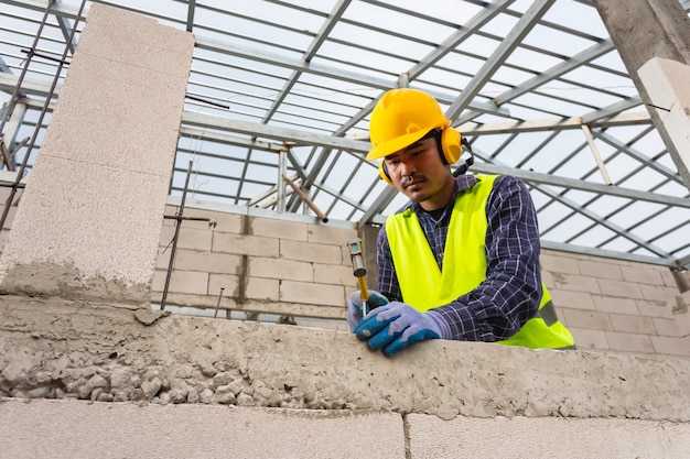 Los trabajadores de la construcción usan un martillo para clavar un clavo de concreto en un bloque de concreto liviano para construir una casa.