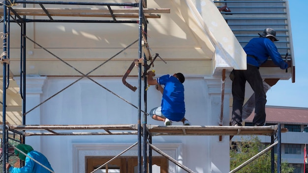 Los trabajadores constructores asiáticos en andamios están trabajando para renovar el antiguo edificio de la casa