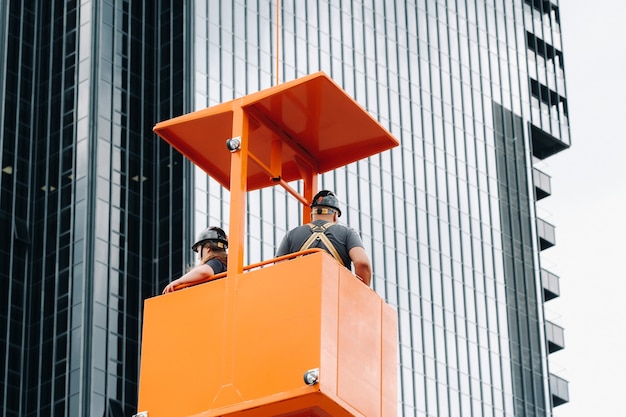 Los trabajadores de una cuna de construcción se suben a una grúa hasta un gran edificio de cristal.