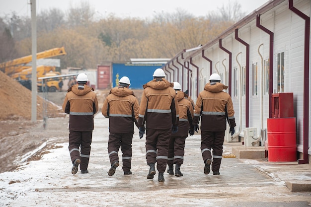 Trabajadores en equipos especiales y cascos con construcción de petróleo y gas en segundo plano.