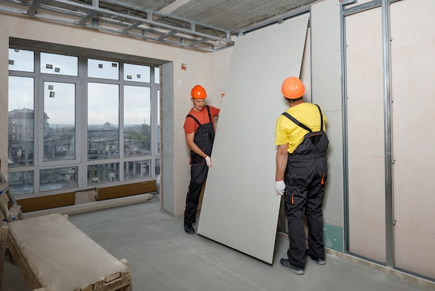 Los trabajadores están montando una placa de yeso en la pared.