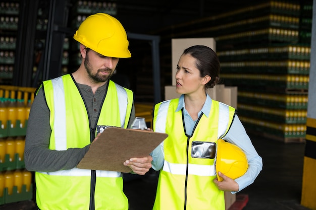 Trabajadores de fábrica discutiendo inventario sobre portapapeles