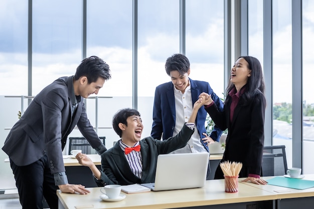 Trabajadores felices exitosos Grupo de empresarios asiáticos con diversos géneros (LGBT) Aplauda y felicita al empresario homosexual ver un plan de negocios exitoso en la computadora portátil en el m