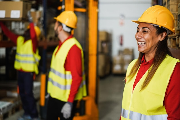Trabajadores industriales cargando cajas de entrega dentro del almacén Enfoque en el casco de mujer latina