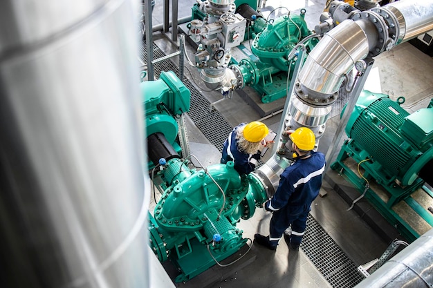 Trabajadores industriales parados en una plataforma de refinería revisando tuberías de gas y generadores de motores