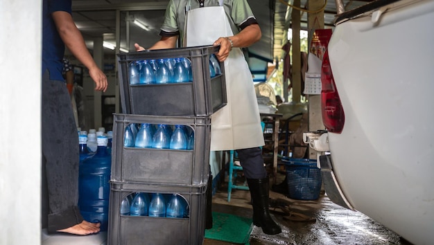 Los trabajadores levantan galones de agua potable azul y botellas en cajas en la parte trasera de un camión de transporte