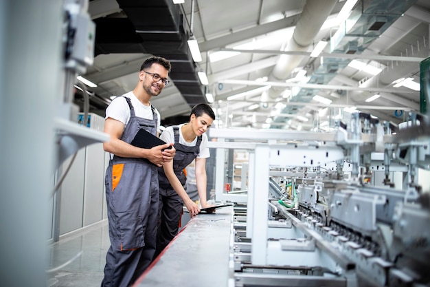 Los trabajadores de la línea de producción que controlan el proceso de envasado de la máquina industrial en la fábrica de impresión