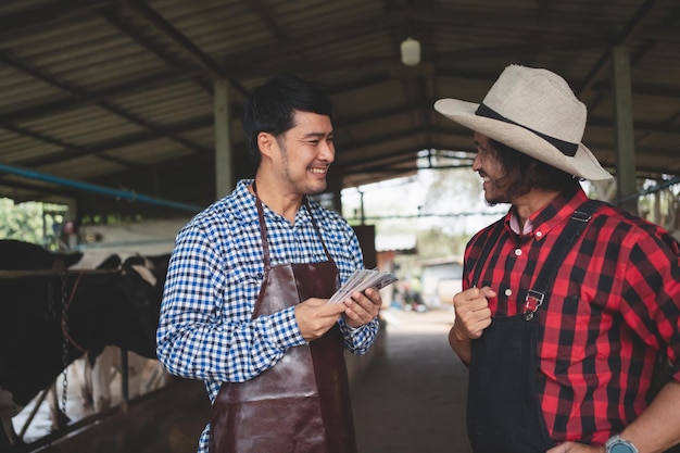 Los trabajadores masculinos pagan dinero y dan la mano a los granjeros en la granja lecheraIndustria agrícola concepto de agricultura y ganadería Vaca en la granja lechera comiendo heno Pequeña empresa de establo