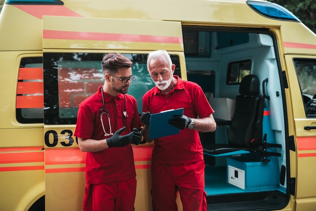 Trabajadores masculinos del servicio médico de emergencia de pie y posando delante del coche de la ambulancia.