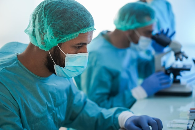 Trabajadores médicos con traje hazmat que trabajan con computadora y microscopio dentro del hospital de laboratorio durante el brote de coronavirus - Enfoque en la cara del médico