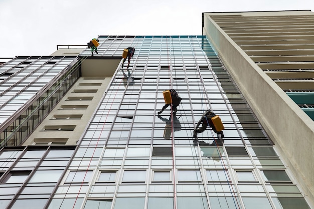 Trabajadores de montañismo industrial se cuelga sobre un edificio de fachada residencial mientras lava el acristalamiento de la fachada exterior. Trabajadores de acceso mediante cuerdas cuelgan de la pared de la casa. Concepto de industria de obras urbanas. Copia espacio