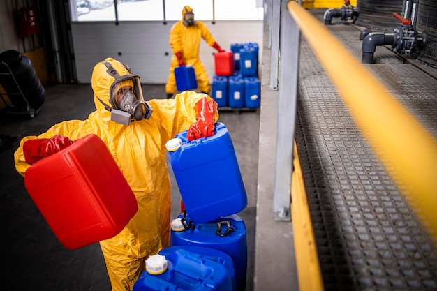 Trabajadores de plantas químicas que transportan envases de plástico con productos químicos o ácidos dentro de la fábrica de producción