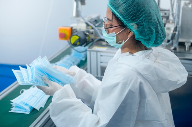 Trabajadores que producen mascarilla quirúrgica en fábrica moderna, protección Covid-19 y concepto médico.