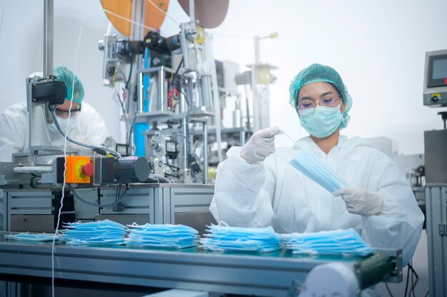 Trabajadores que producen mascarilla quirúrgica en fábrica moderna, protección Covid-19 y concepto médico.