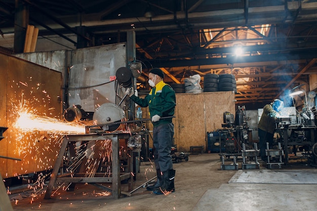 Trabajadores que trabajan con construcción de metal en la planta Procesamiento de metales con sierra de disco de amoladora angular grande y soldadura de soldador Chispas en la metalurgia en la fábrica