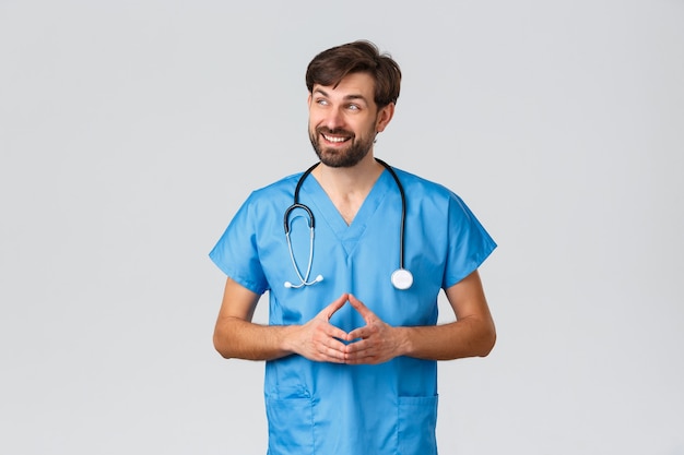 Trabajadores de la salud, campaña de cuarentena de coronavirus y concepto de pandemia. Sonriente médico pationate con batas azules y un estetoscopio, mirando hacia otro lado, pensando, explicando cómo trabajar con personas enfermas a los pasantes.