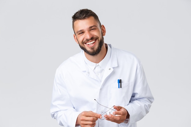 Trabajadores de la salud, coronavirus, pandemia de covid-19 y concepto de seguro. Médico alegre en batas blancas, gafas de despegue, riendo y sonriendo amigablemente al paciente, médico disfrutando de su trabajo.