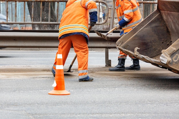 Foto los trabajadores del servicio de carreteras con uniformes reflectantes de color naranja brillante usan palas para quitar la arena acumulada