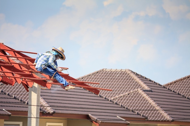 Trabajadores del soldador de la construcción que instalan la estructura del marco de acero del techo de la casa en el sitio de construcción del edificio con nubes y cielo