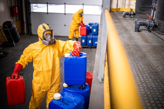 Trabajadores con traje de protección amarillo y máscara de gas que preparan ácidos y productos químicos para la industria metalúrgica