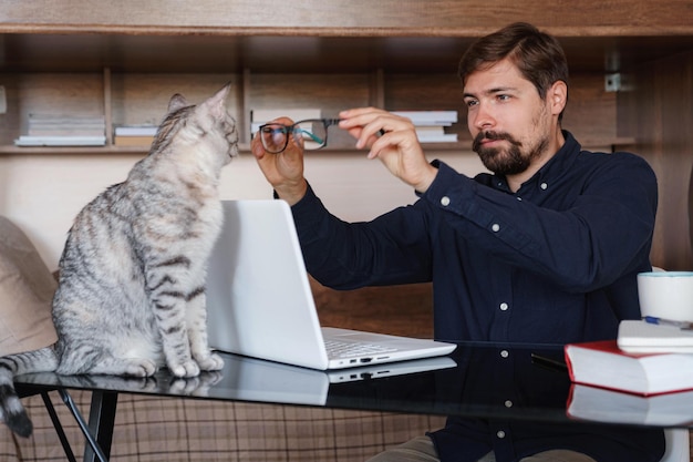 Foto trabajando en casa con una mascota acostada en el regazo el hombre trabaja desde casa escribiendo en una computadora portátil