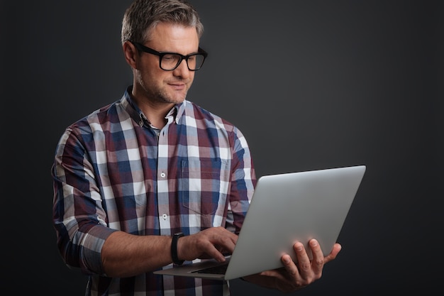 Trabajando desde cualquier lugar. Chico guapo motivado enfocado escribiendo un correo electrónico mientras usa su computadora portátil y usa las gafas