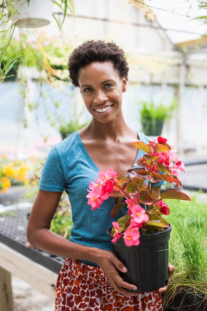 Trabajando en una granja orgánica Una mujer sosteniendo una gran planta con flores una begonia con pétalos de rosa