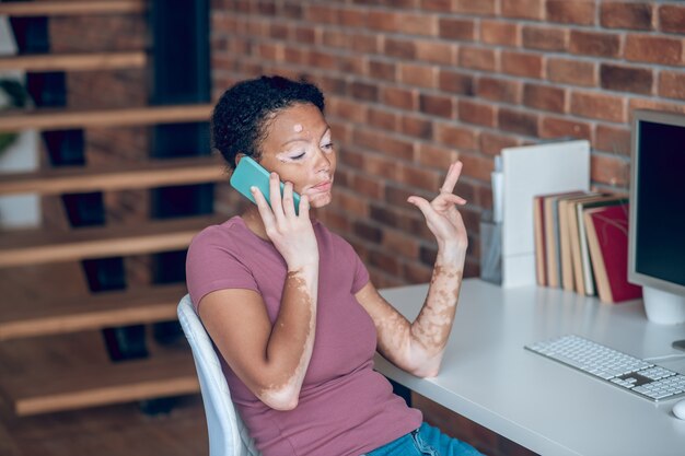 Trabajando. Joven afroamericana hablando por teléfono y mirando ocupado