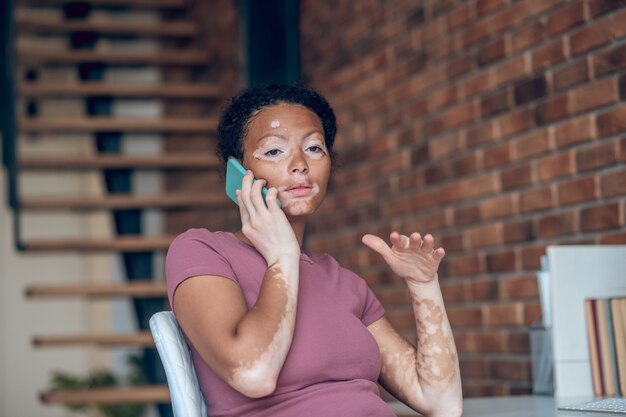 Trabajando. Joven afroamericana hablando por teléfono y mirando ocupado